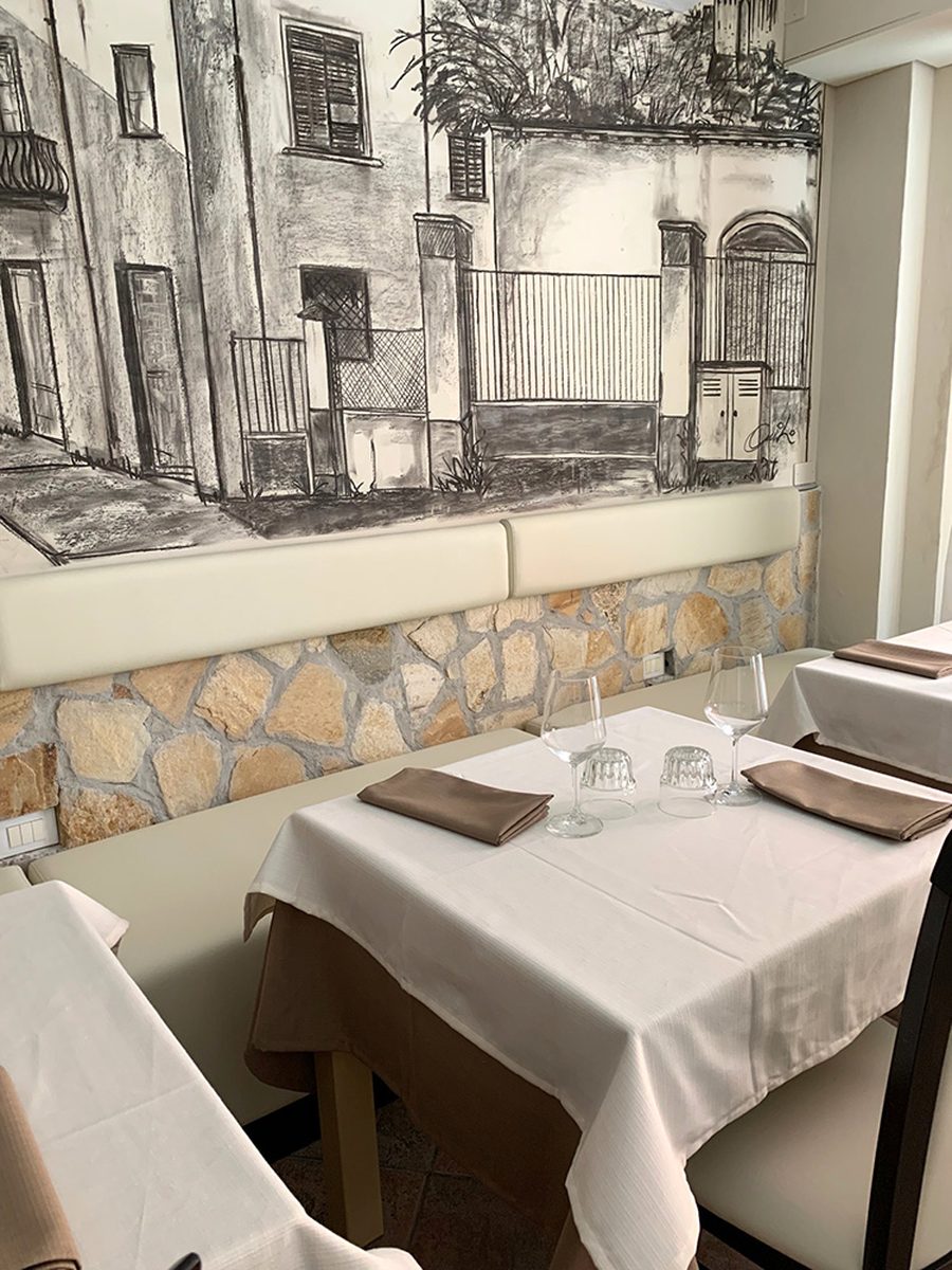 Tavolo apparecchiato accanto alla panca, con il dado in pietra chiara sotto il disegno.