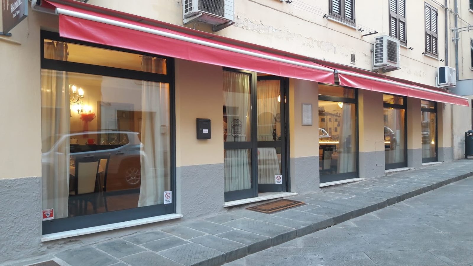 L'ingresso del ristorante in Via Beatrice, con le tende rosse e le vetrine illuminate.